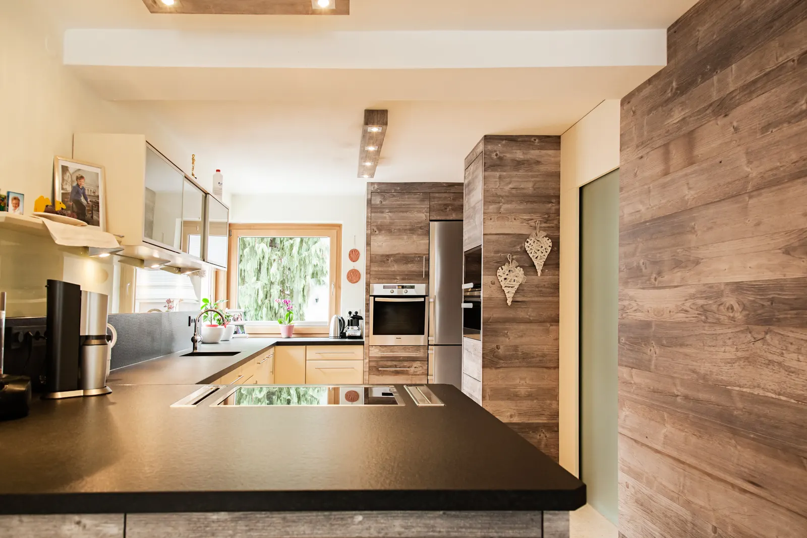 Küche mit dunkler Arbeitsplatte, Kochinsel und Wandverkleidung aus Altholz